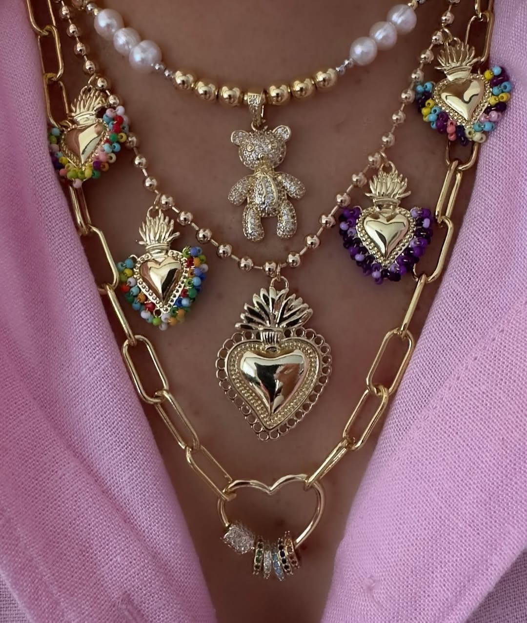 Layered gold jewelry with heart charms and teddy bear pendant.